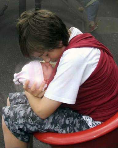 Big brother wrapping newborn baby in a baby wrap.